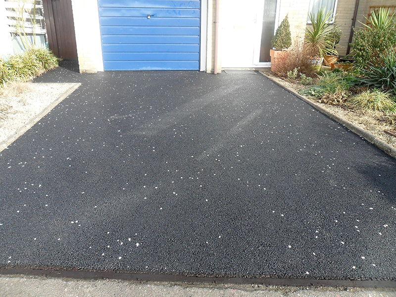 Resurfaced drive with new tarmacadam incorporating white granite chippings.
